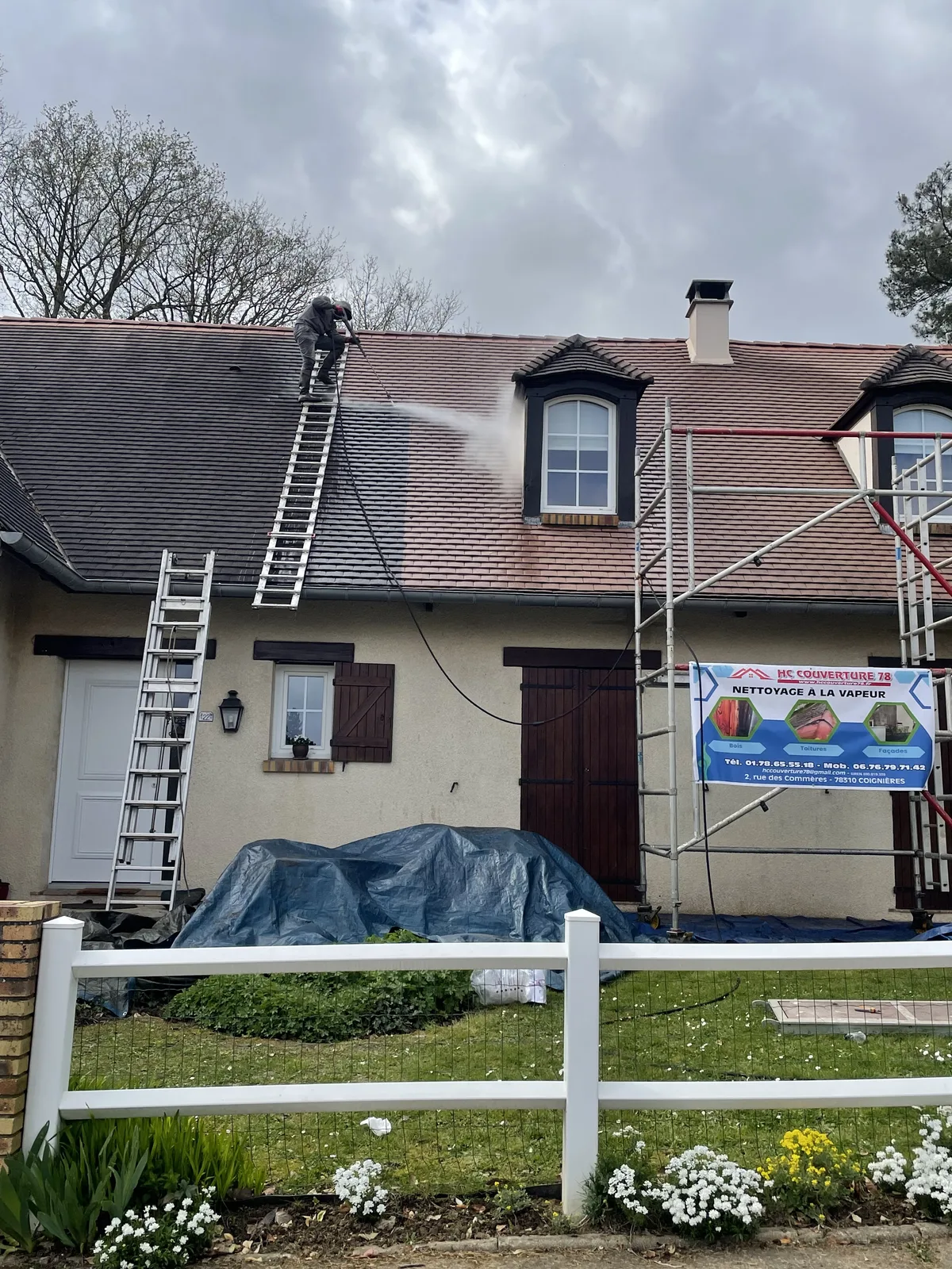 Intervenant sur une échelle de toit appliquant un jet de vapeur sur les tuiles, échafaudage installé devant la maison