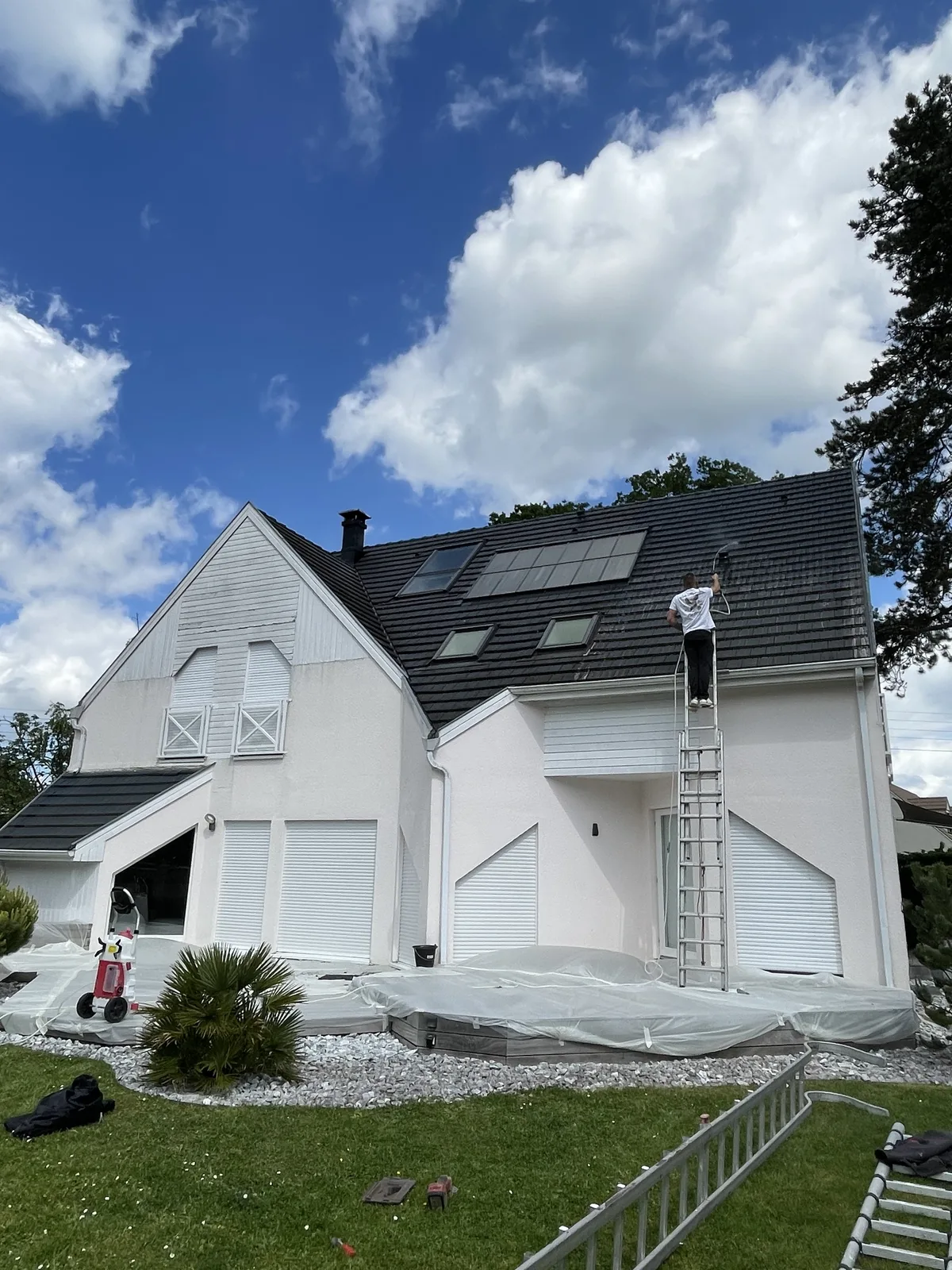 Application d’un hydrofuge sur la toiture d’une maison blanche, avec la terrasse protégée par des bâches